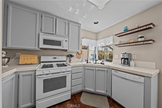 kitchen featuring white appliances, tile counters, dark wood-type flooring, gray cabinetry, and a sink