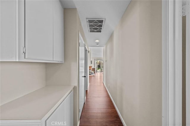 hall with dark wood-style floors, visible vents, and baseboards