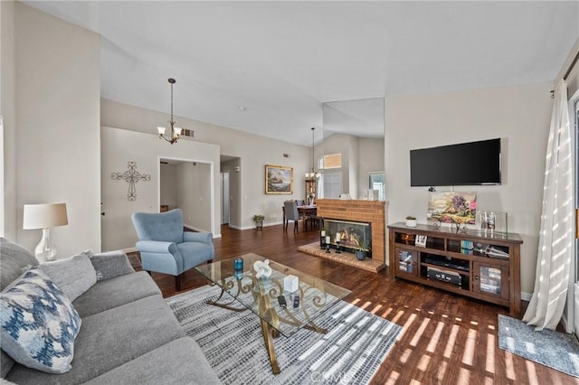 living area featuring an inviting chandelier, a fireplace, vaulted ceiling, and wood finished floors