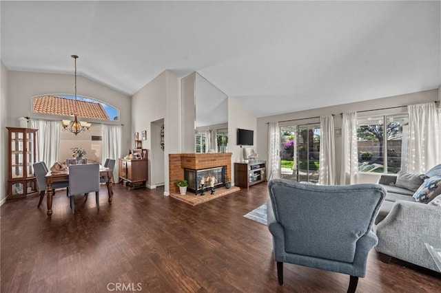 living room featuring lofted ceiling, dark wood finished floors, a notable chandelier, and a brick fireplace