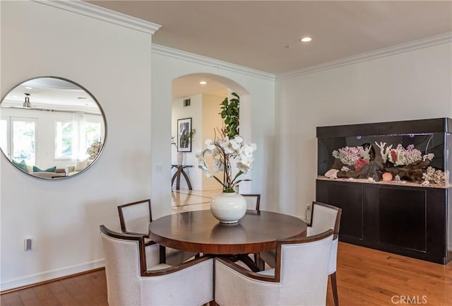 dining room with arched walkways, visible vents, baseboards, light wood-style floors, and crown molding