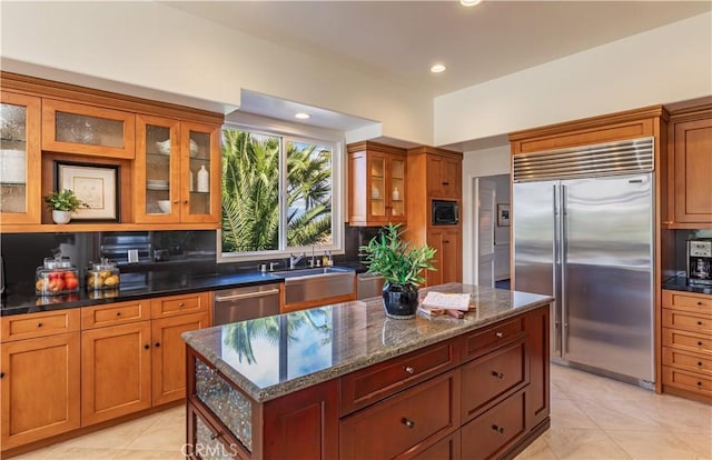 kitchen with decorative backsplash, brown cabinetry, a sink, a kitchen island, and built in appliances