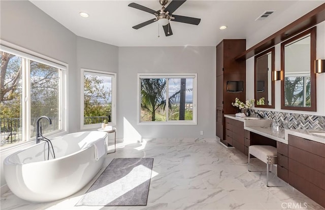 full bath featuring marble finish floor, a freestanding tub, vanity, and recessed lighting