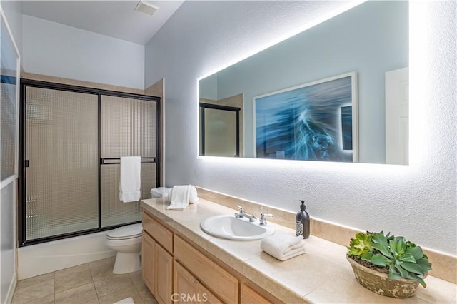 bathroom featuring visible vents, toilet, shower / bath combination with glass door, tile patterned flooring, and vanity