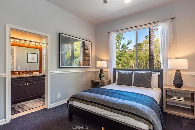 bedroom with baseboards, dark colored carpet, and connected bathroom