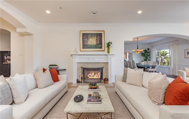 living area with arched walkways, a notable chandelier, crown molding, recessed lighting, and a premium fireplace