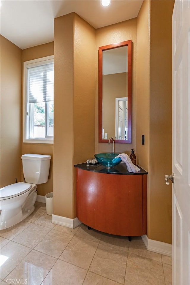 half bathroom with baseboards, vanity, toilet, and tile patterned floors