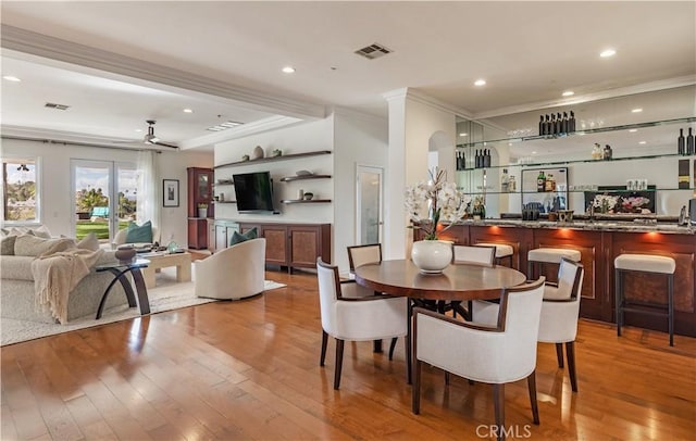 dining space with indoor wet bar, crown molding, wood-type flooring, visible vents, and a ceiling fan