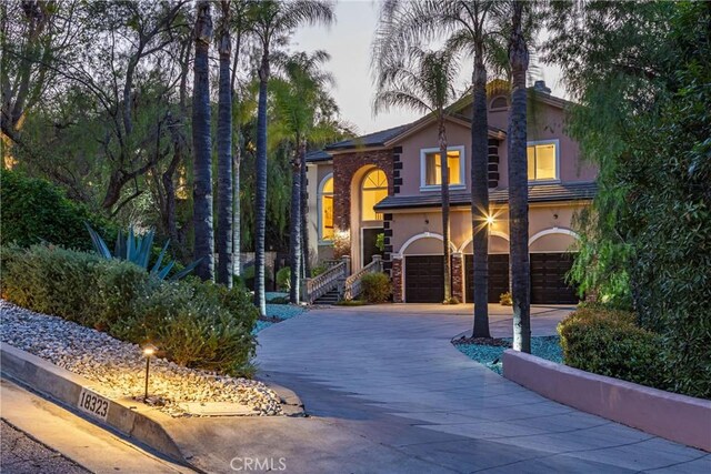 view of front of house with stone siding, driveway, an attached garage, and stucco siding