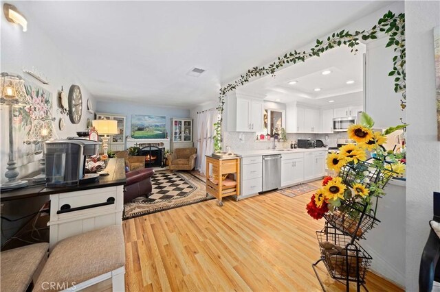 kitchen featuring a warm lit fireplace, a sink, open floor plan, appliances with stainless steel finishes, and light wood-type flooring