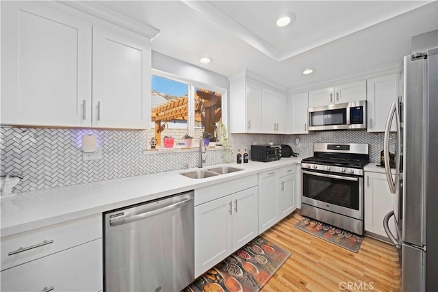 kitchen with light wood finished floors, appliances with stainless steel finishes, a sink, and white cabinetry