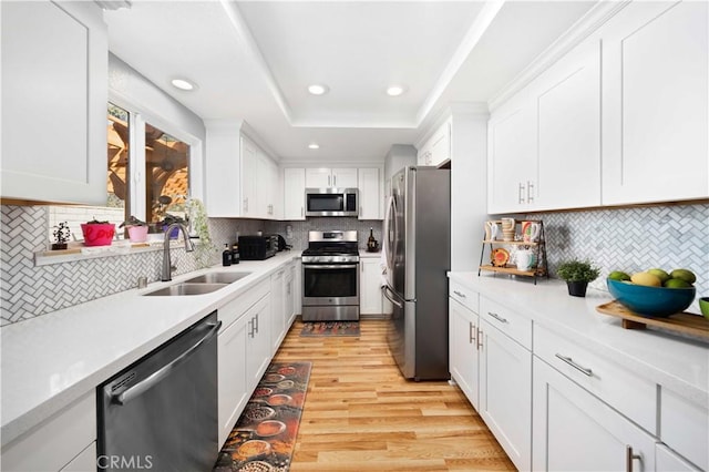 kitchen featuring a raised ceiling, stainless steel appliances, light wood-type flooring, white cabinetry, and a sink