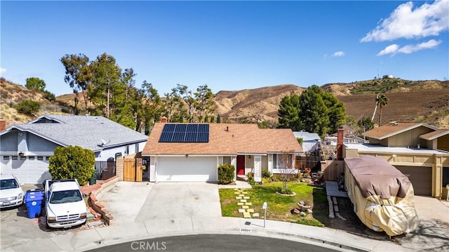 ranch-style home featuring a garage, fence, a gate, and roof mounted solar panels