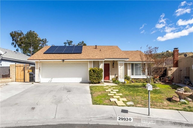 ranch-style home featuring driveway, solar panels, an attached garage, fence, and a front lawn