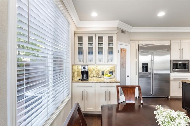 kitchen featuring visible vents, light stone counters, tasteful backsplash, crown molding, and built in appliances