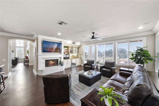 living area with visible vents, ornamental molding, a high end fireplace, arched walkways, and dark wood-style flooring