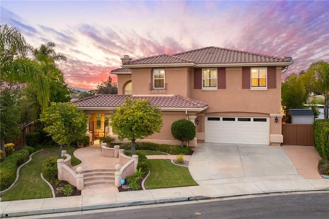 mediterranean / spanish home with stucco siding, an attached garage, driveway, and fence