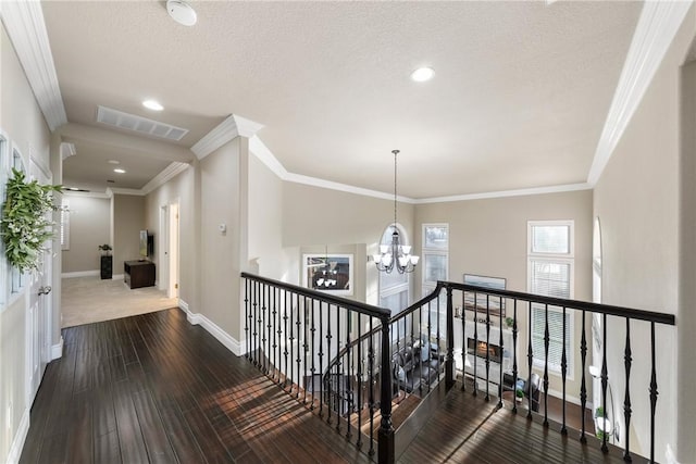 corridor featuring wood finished floors, baseboards, visible vents, an inviting chandelier, and ornamental molding