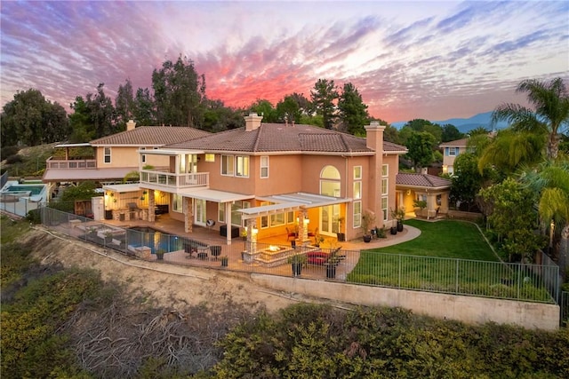 back of property at dusk with stucco siding, a chimney, a yard, a balcony, and a fenced backyard