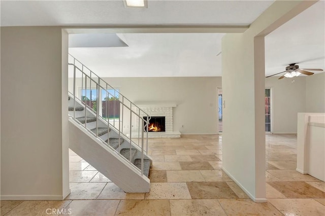 interior space featuring a ceiling fan, a fireplace, baseboards, and stone tile flooring