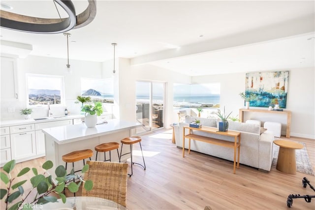 interior space featuring light wood finished floors, a kitchen island, beam ceiling, light countertops, and white cabinets