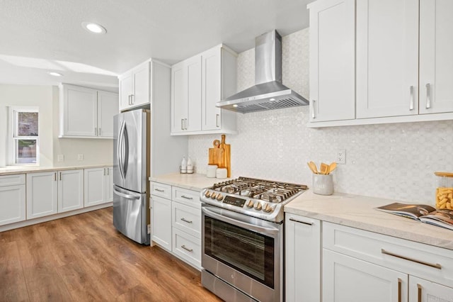 kitchen with stainless steel appliances, wood finished floors, white cabinets, light stone countertops, and wall chimney exhaust hood