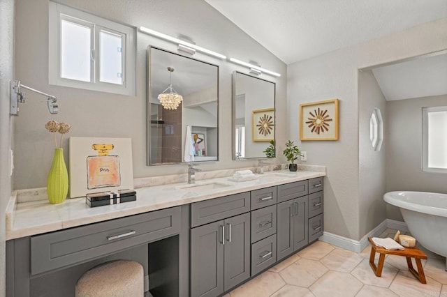 full bath featuring double vanity, a freestanding bath, a healthy amount of sunlight, vaulted ceiling, and a sink