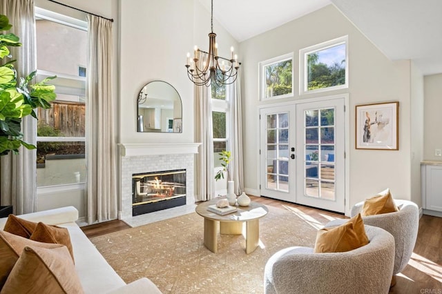 sitting room featuring a tiled fireplace, wood finished floors, an inviting chandelier, french doors, and high vaulted ceiling