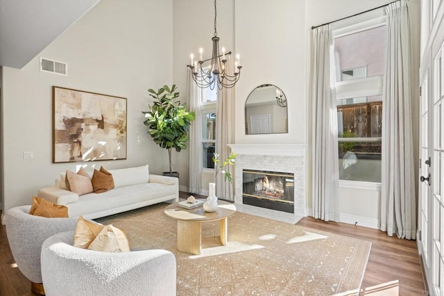 living room with visible vents, a towering ceiling, a fireplace with flush hearth, wood finished floors, and a chandelier