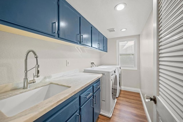 clothes washing area with dark wood-style flooring, washing machine and clothes dryer, cabinet space, visible vents, and a sink