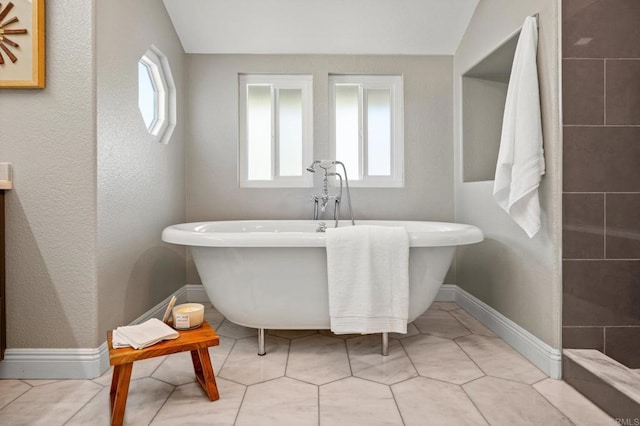 bathroom with lofted ceiling, a soaking tub, tile patterned floors, and baseboards