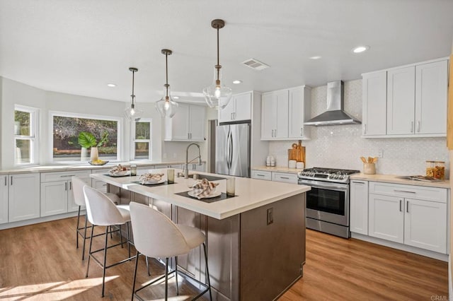 kitchen featuring stainless steel appliances, a sink, visible vents, light wood-type flooring, and wall chimney exhaust hood