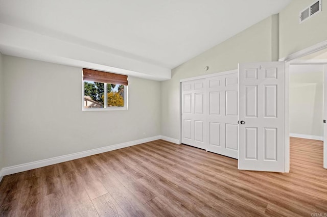 unfurnished bedroom featuring wood finished floors, visible vents, baseboards, vaulted ceiling, and a closet