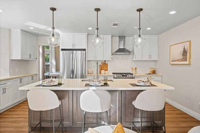 kitchen with decorative backsplash, freestanding refrigerator, wall chimney range hood, light wood-type flooring, and range