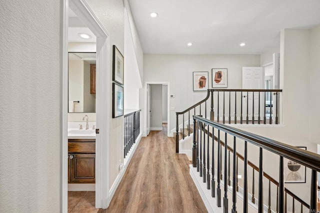 hallway featuring baseboards, stairway, wood finished floors, a sink, and recessed lighting