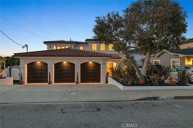 mediterranean / spanish-style house featuring a gate, a tile roof, and stucco siding