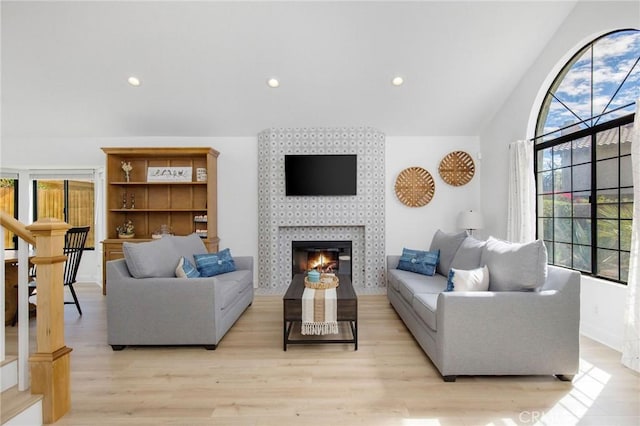 living area with lofted ceiling, recessed lighting, a tiled fireplace, light wood-style floors, and stairs