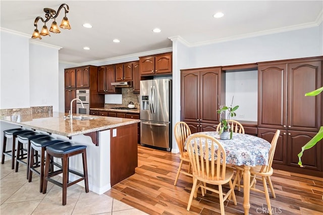 kitchen with under cabinet range hood, stainless steel appliances, a peninsula, a sink, and decorative backsplash