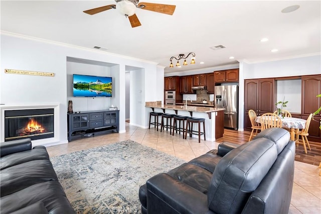 living room with ornamental molding, a glass covered fireplace, visible vents, and light tile patterned floors