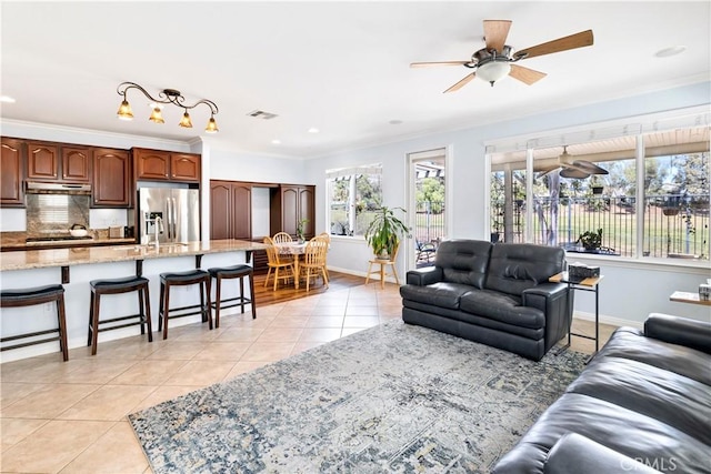 living room featuring light tile patterned floors, baseboards, visible vents, ceiling fan, and crown molding