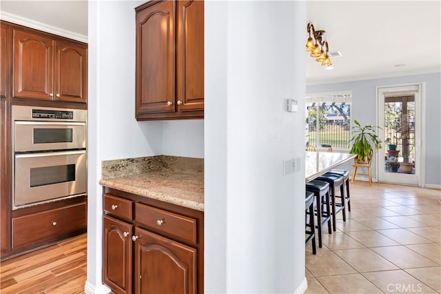 kitchen featuring light tile patterned floors, baseboards, ornamental molding, light stone counters, and double oven