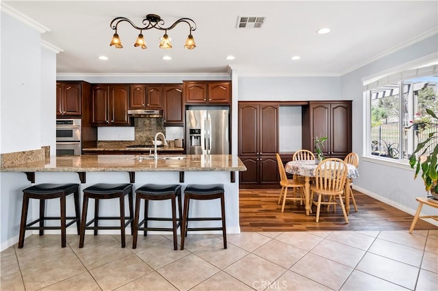 kitchen featuring appliances with stainless steel finishes, ornamental molding, under cabinet range hood, and tasteful backsplash