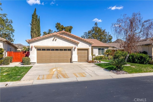 mediterranean / spanish-style home featuring an attached garage, fence, driveway, a tiled roof, and stucco siding