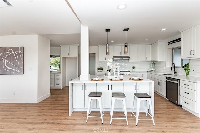 kitchen featuring visible vents, stainless steel dishwasher, a sink, light wood-type flooring, and under cabinet range hood