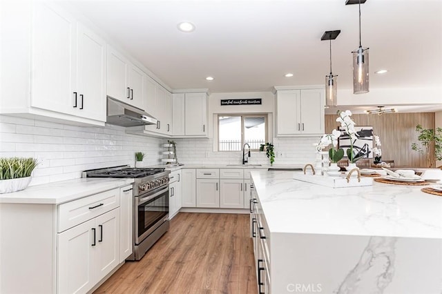 kitchen with high end stainless steel range oven, white cabinets, a kitchen island with sink, light wood-type flooring, and under cabinet range hood