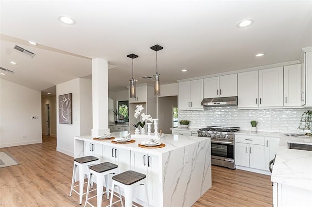 kitchen with visible vents, backsplash, high end range, and under cabinet range hood