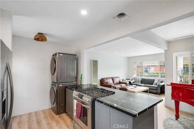kitchen with stainless steel appliances, open floor plan, a peninsula, light wood-type flooring, and stacked washer and clothes dryer
