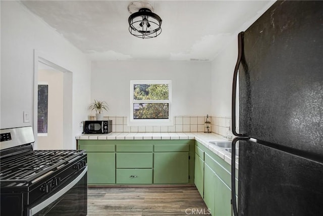 kitchen featuring tile countertops, green cabinetry, light wood finished floors, and black appliances