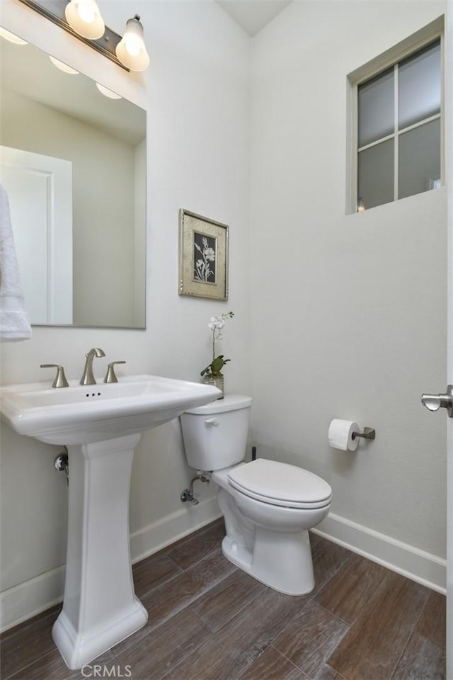 half bath with toilet, a sink, baseboards, and wood finished floors