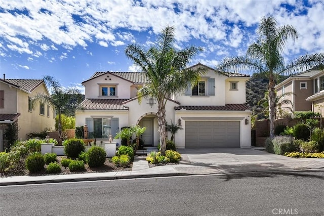 mediterranean / spanish-style home with driveway, an attached garage, a tile roof, and stucco siding